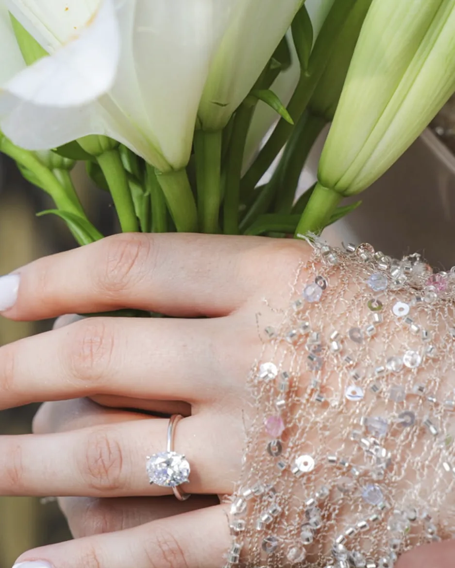 Hand der Braut mit Verlobungsring an einem Strauß weißer Lilien